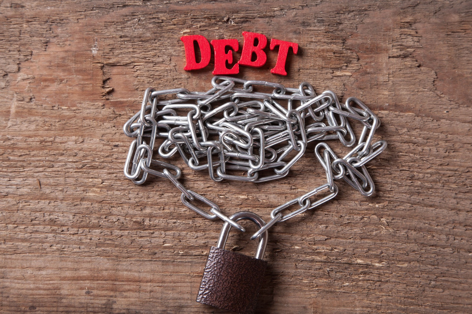 Debt of red letters near the chain with a closed lock on the wood background.